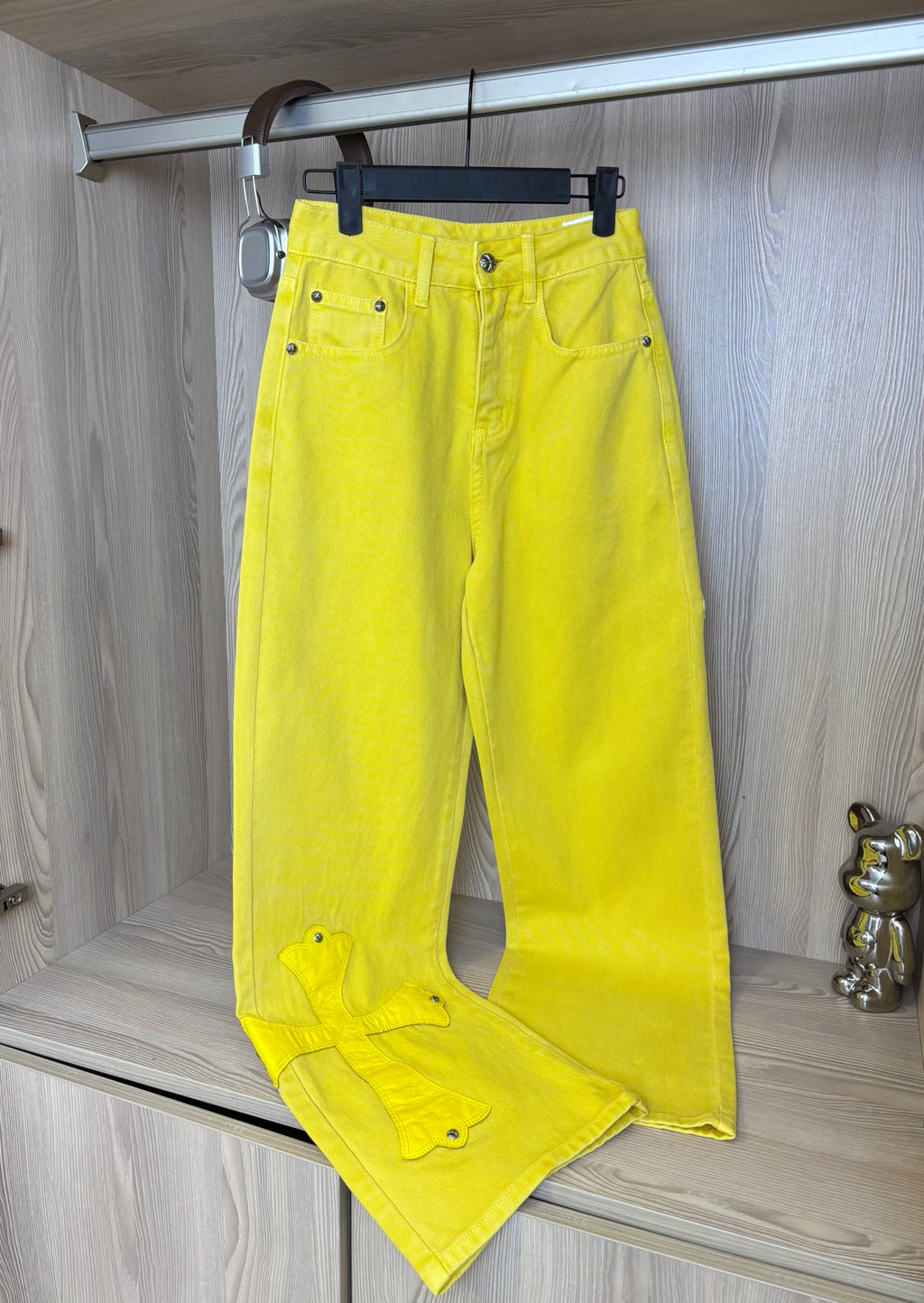 Bright yellow pants with front button closure and cross patches, hanging on a rack.