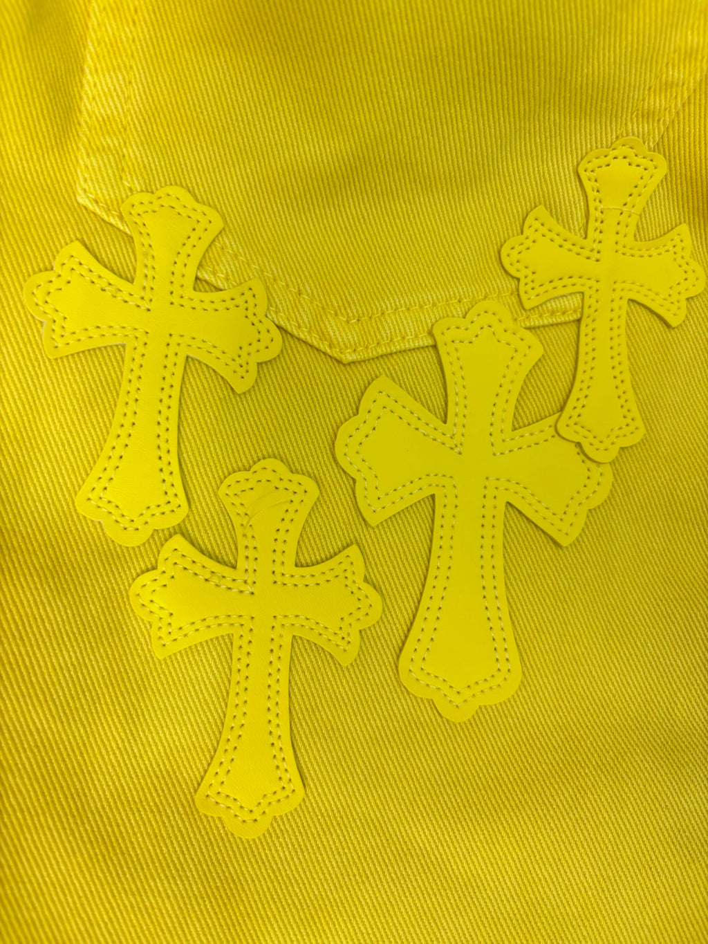 Embroidered cross appliqués on bright yellow fabric panel.
