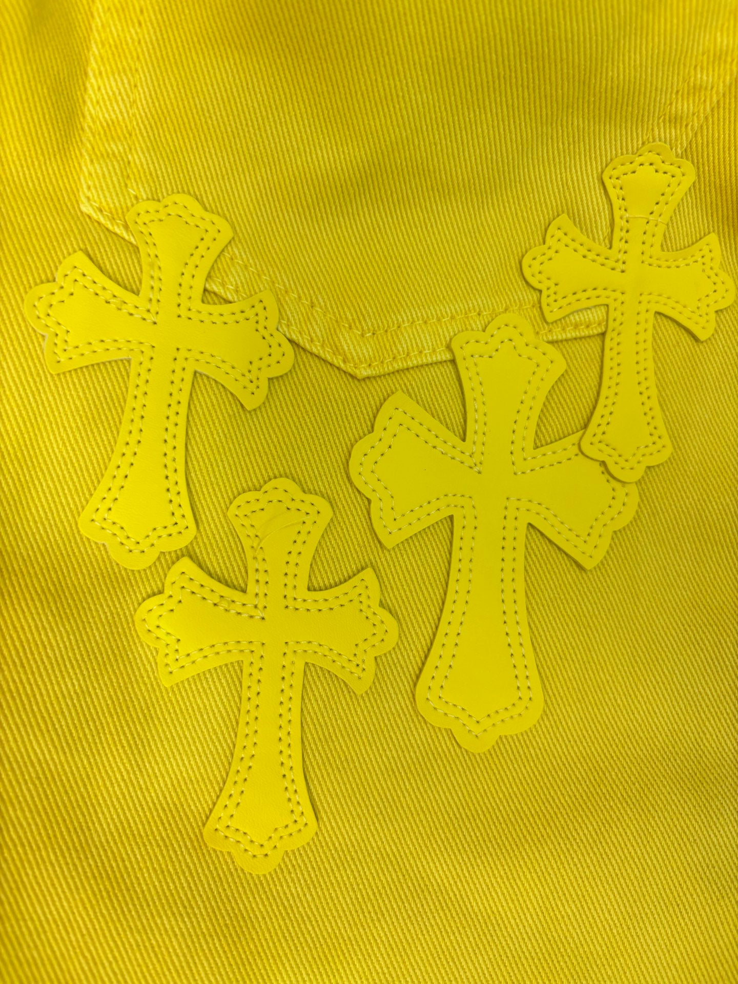 Embroidered cross appliqués on bright yellow fabric panel.
