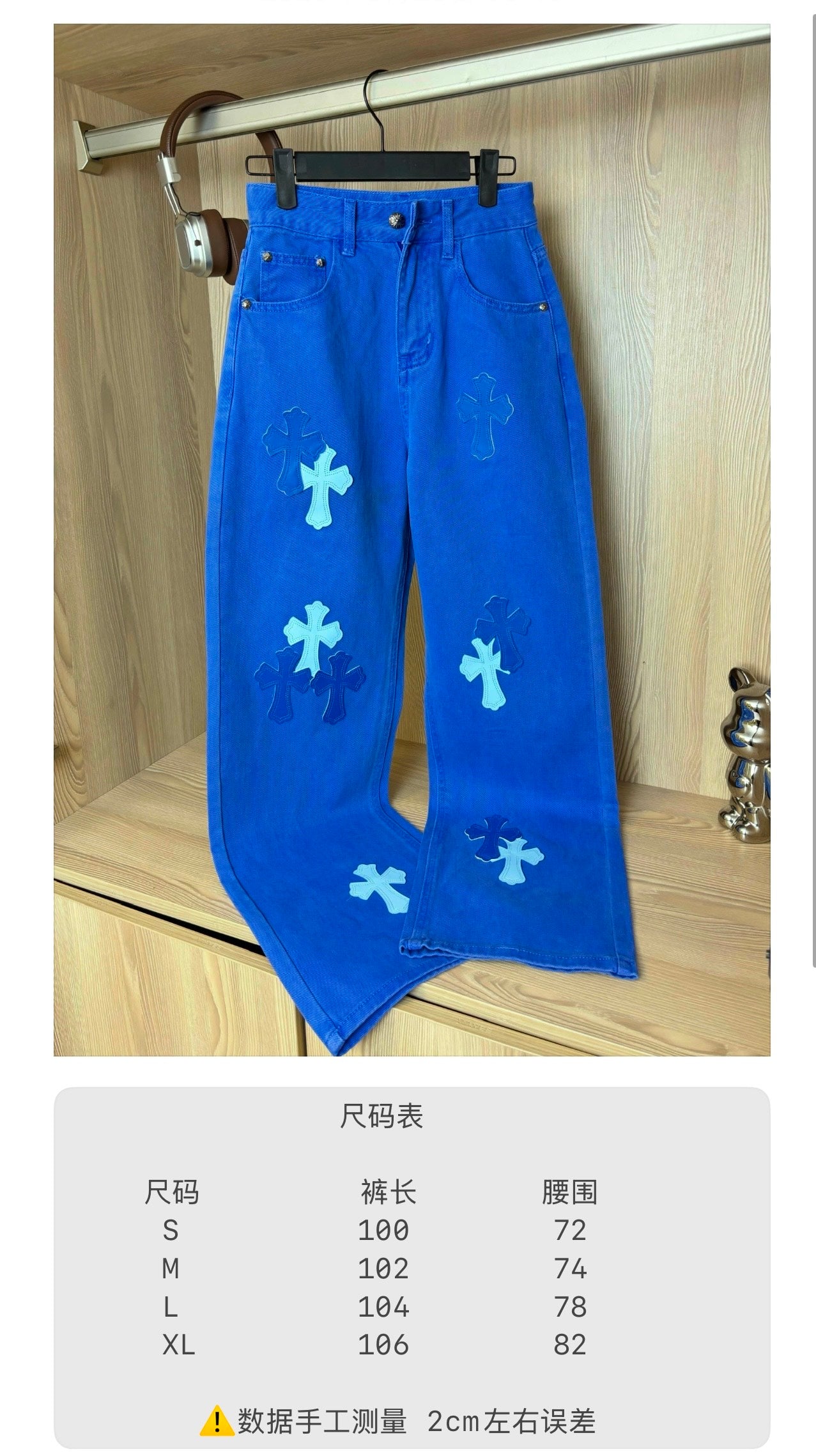 Blue denim pants with white cross appliqué, hanging on a closet bar