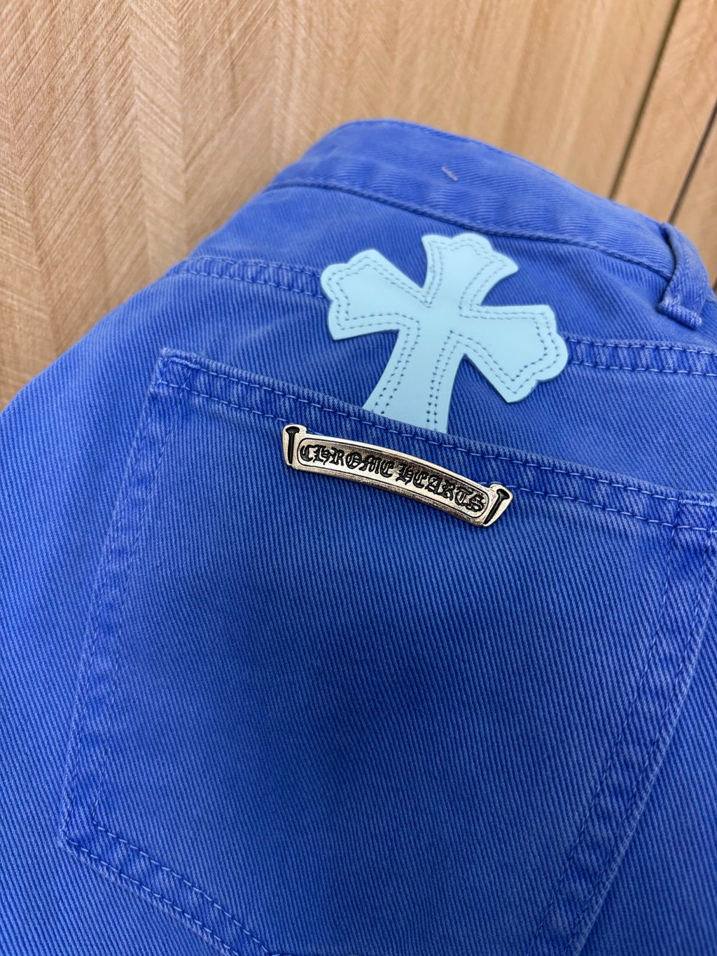 Blue denim pants with large white cross patch and metal logo label
