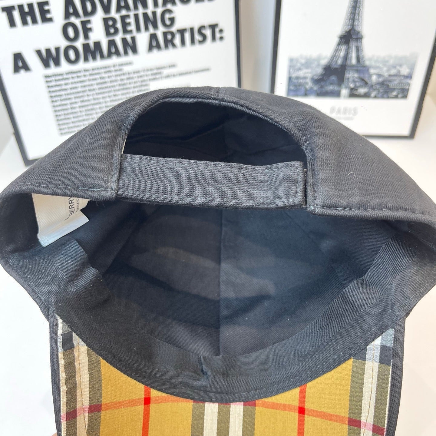 Black Burberry cap interior with curved brim and stitched seam around the opening.