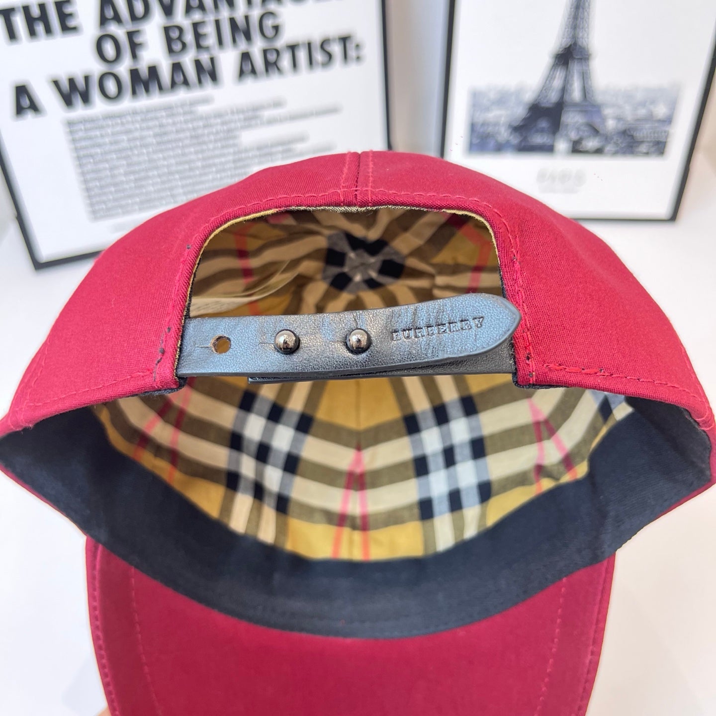 Burberry cap interior view with plaid lining and metal adjuster strap across the top