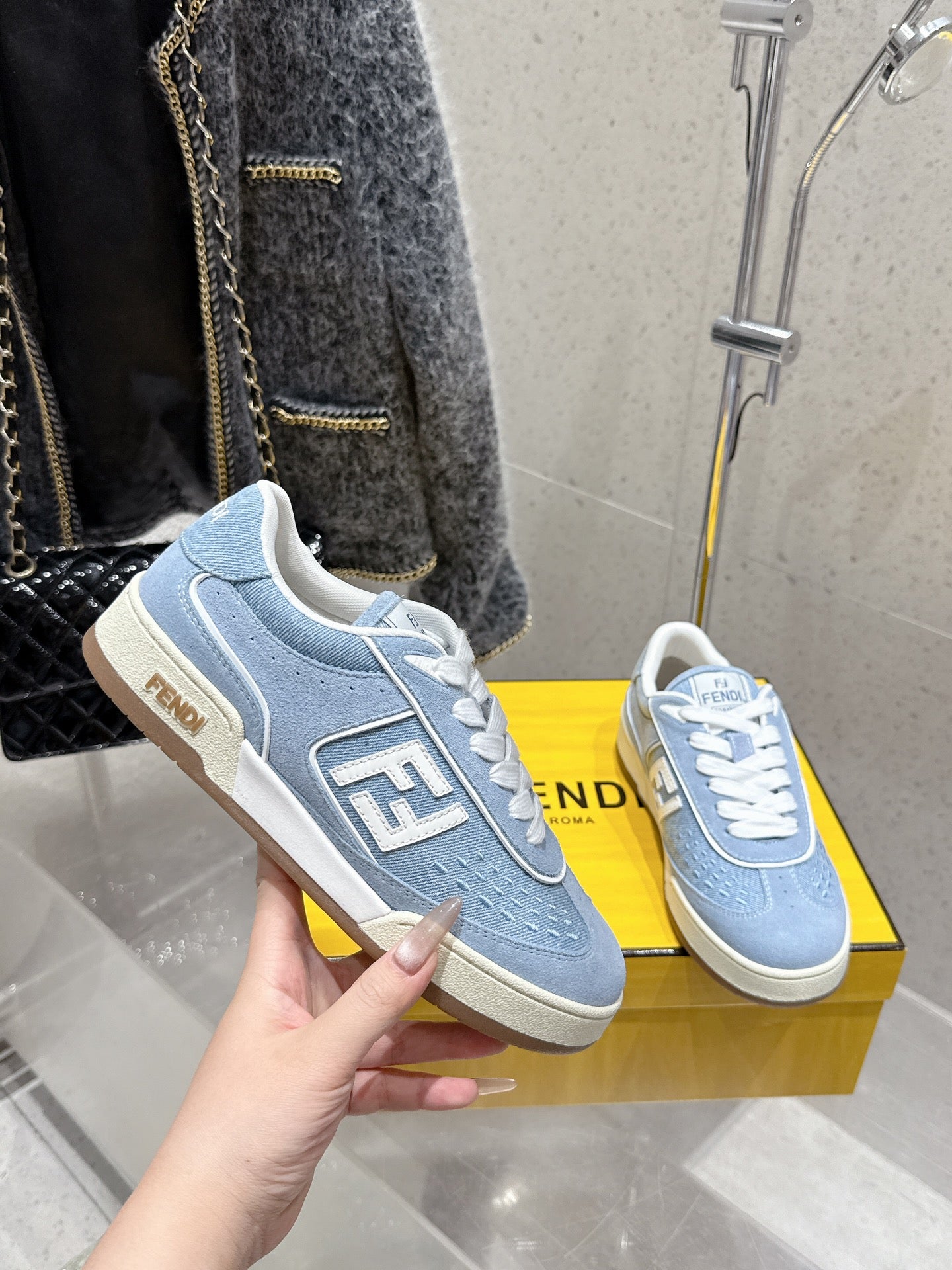 Light blue Fendi sneakers held in hand, white laces and F side logo