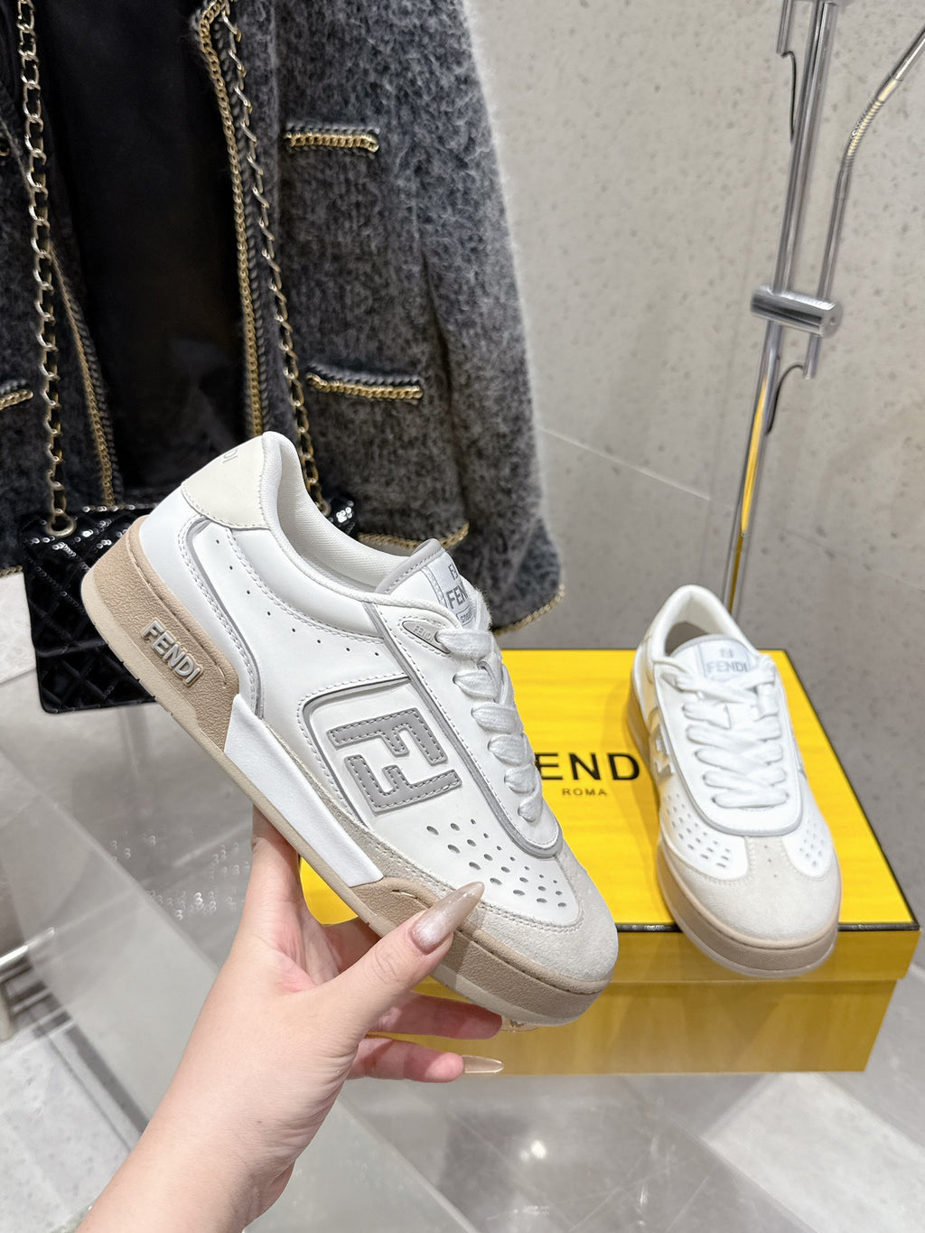 White Fendi sneaker held in hand, FF logo side and lace-up upper