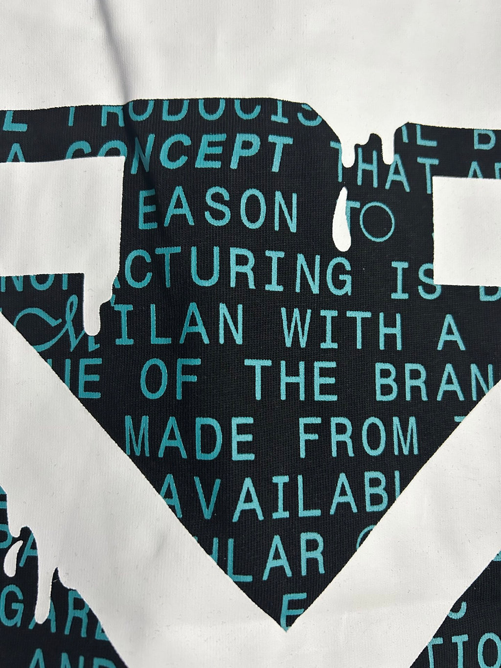 Black crewneck T-shirt close-up of white X emblem over teal text.