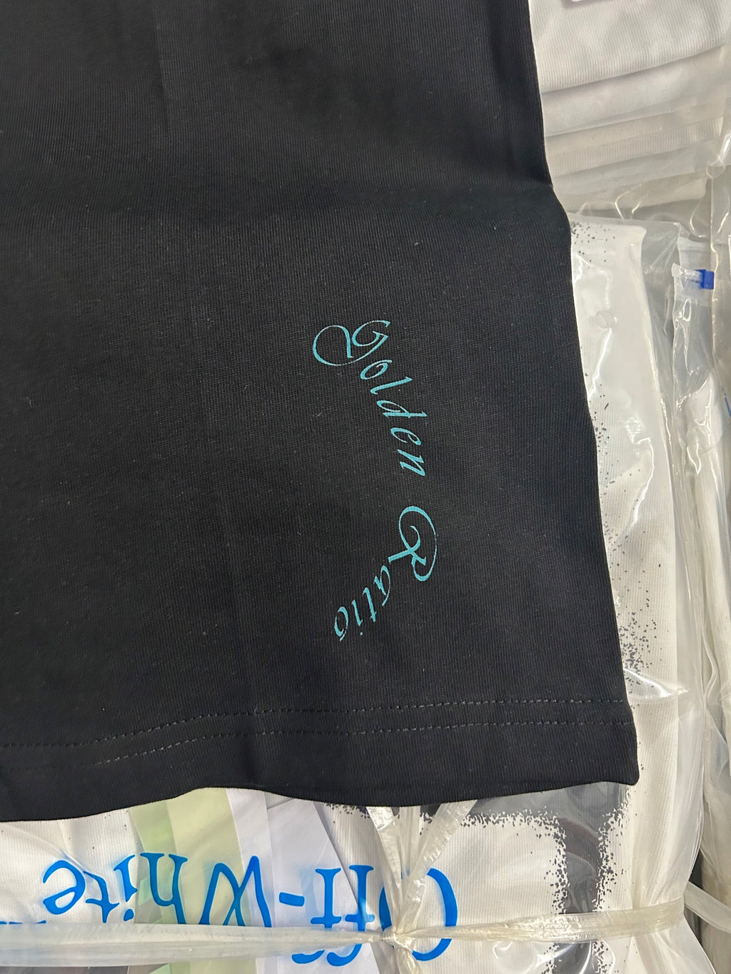 Black T-shirt hem with small teal signature-style embroidery on the side.