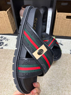 Gucci black slide sandals side view, diagonal green red web strap and badge