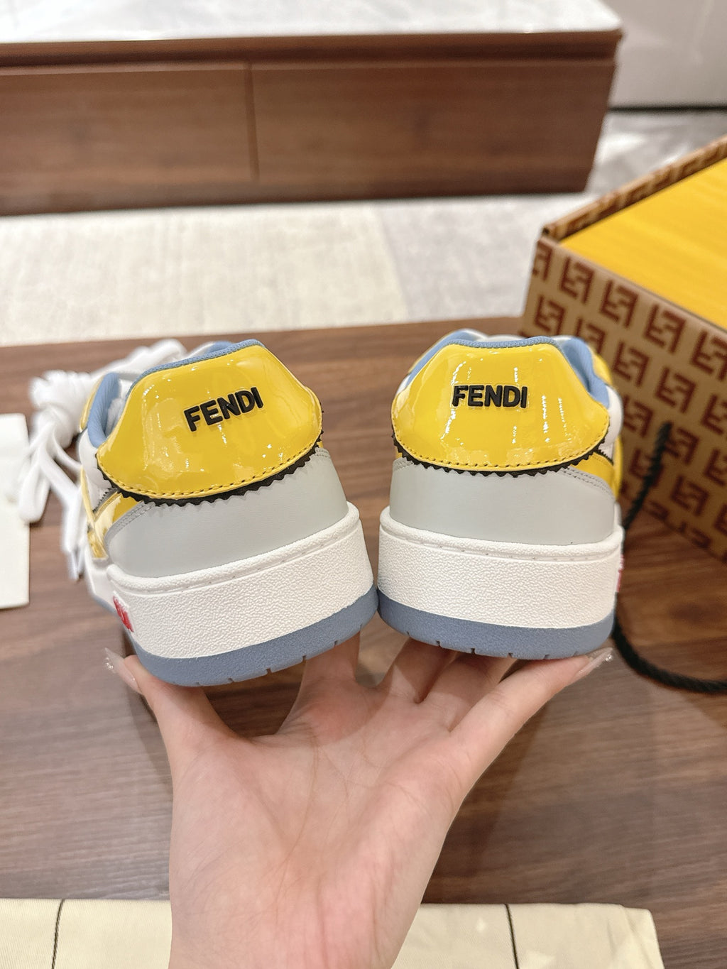 Back view of low-top sneakers, white with yellow heel tabs, blue rubber soles