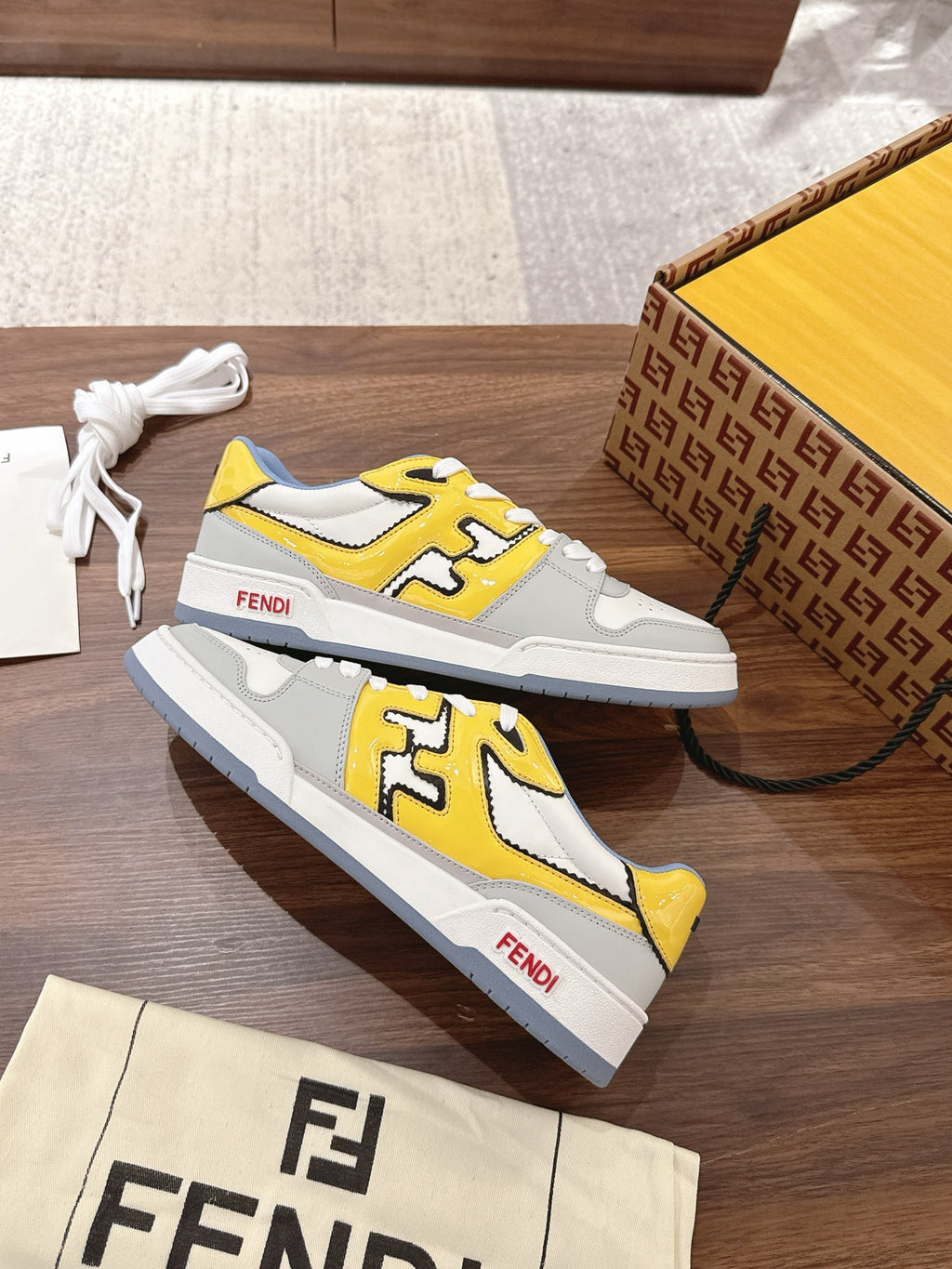Low-top sneakers with white uppers and yellow logo details, displayed with shoe box