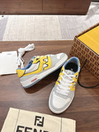White low-top sneakers with yellow logo trim and blue heel lining, box and dust bag