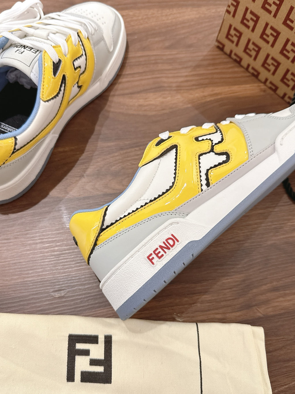 Single low-top sneaker, white with yellow logo panel and blue collar, side view
