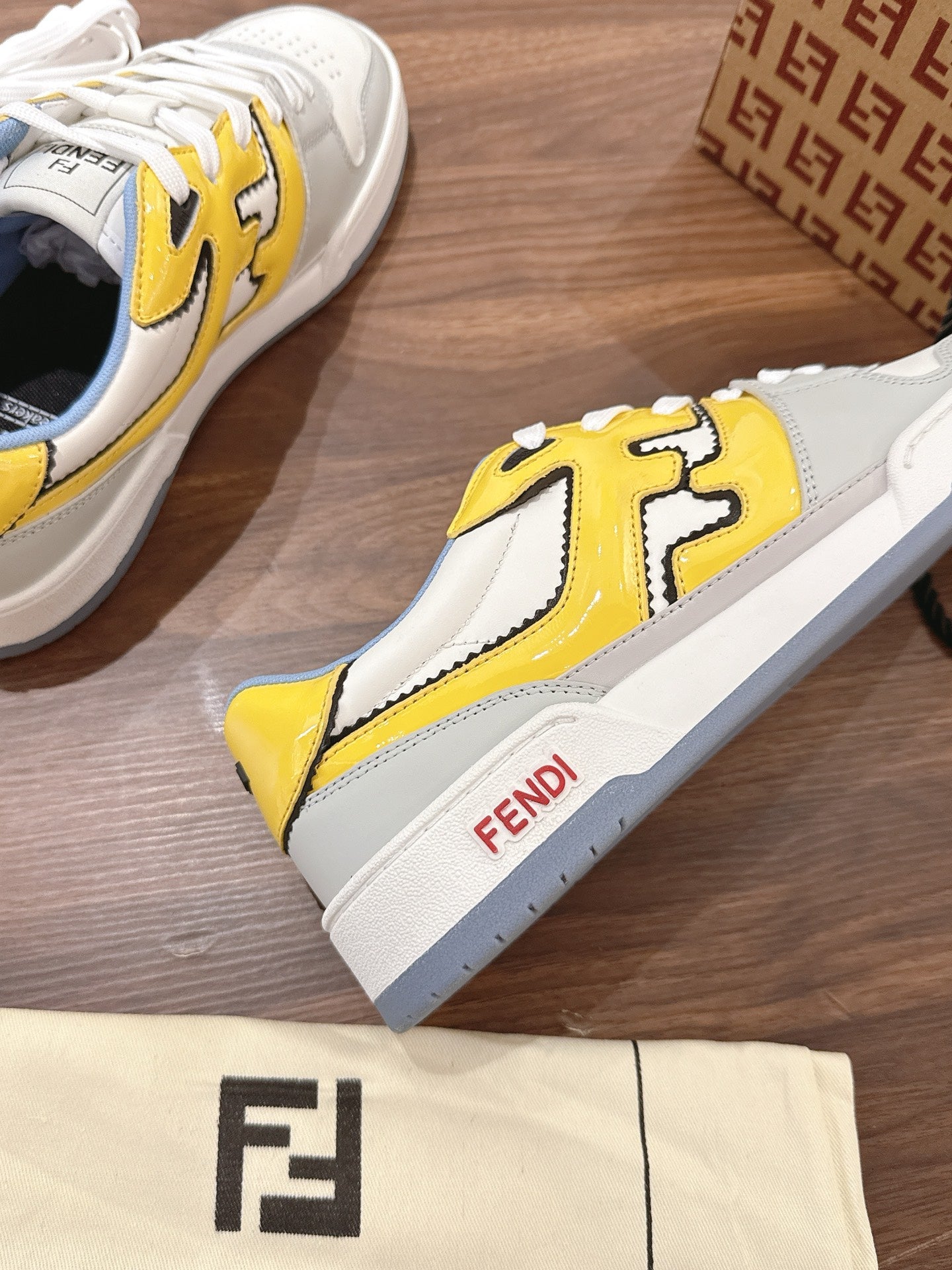 Single low-top sneaker, white with yellow logo panel and blue collar, side view