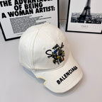 White Balenciaga cap angled view with embroidered cartoon patch and BALENCIAGA logo