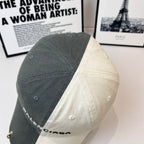 Two-tone baseball cap, dark gray crown and off-white side panel, rear stitching detail.