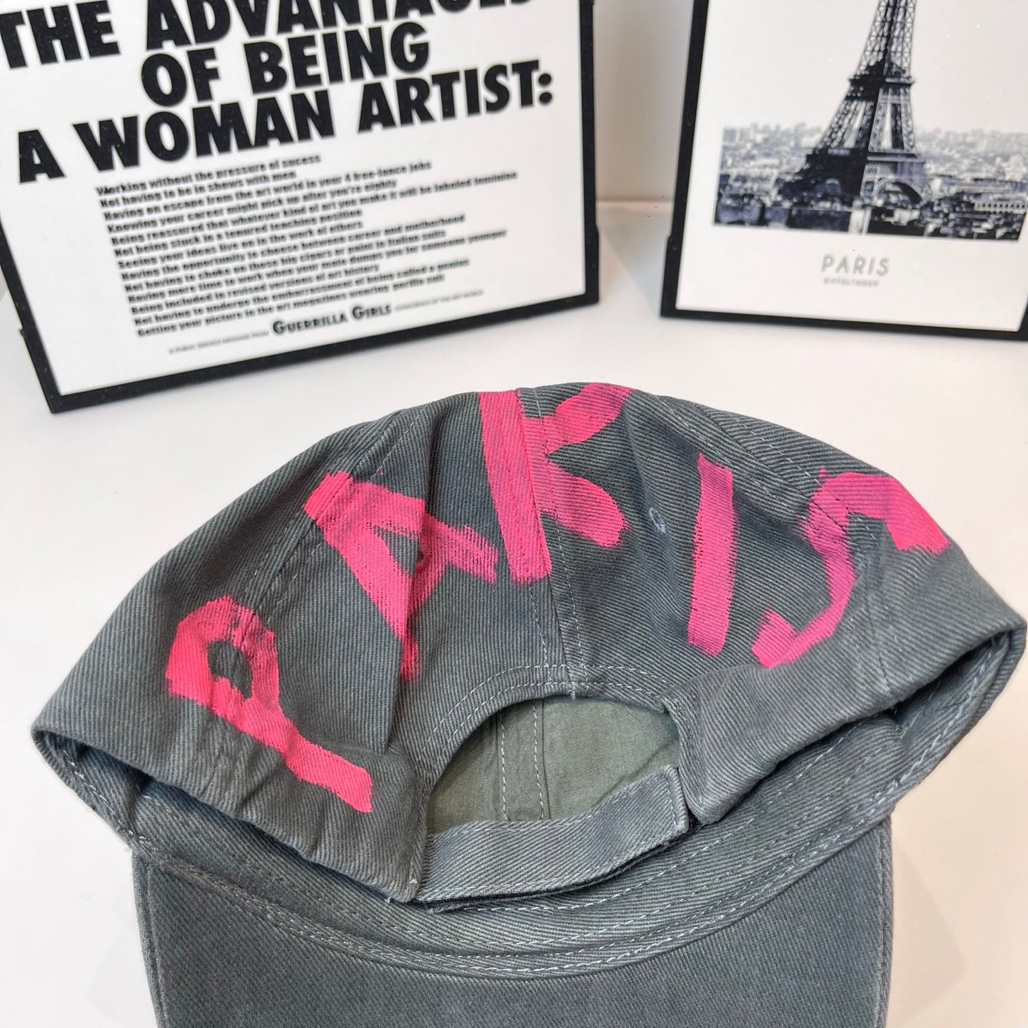 Baseball cap, dark gray with pink letters on back of crown and curved brim.