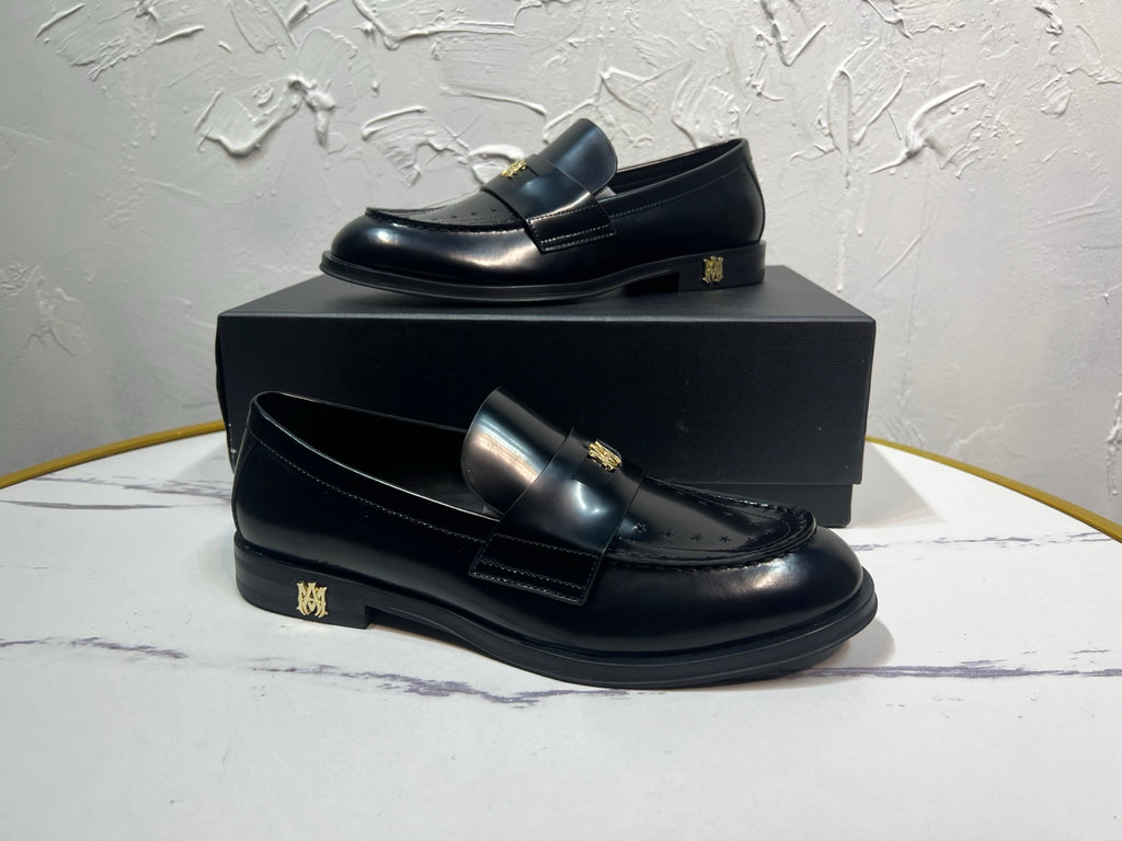 Amiri black leather loafer pair with gold emblem detail, side view on box
