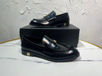 Amiri black leather loafer pair with gold emblem detail, side view on box