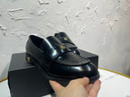 Amiri black leather loafer shoe held in hand, gold emblem strap, close-up