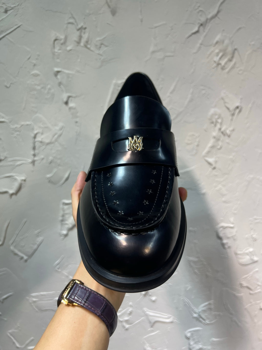 Amiri black leather loafer with gold emblem on upper, heel view held up