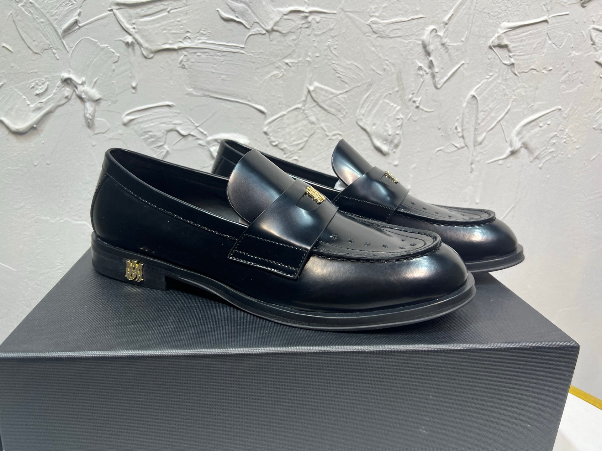 Amiri black leather loafers with gold emblem strap, front three-quarter view