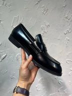 Amiri black leather loafer with gold emblem strap, held shoe side profile