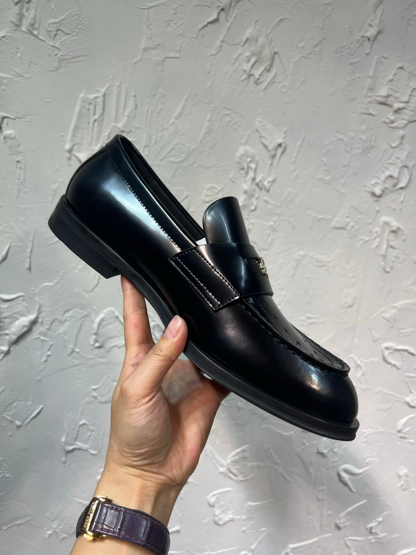 Amiri black leather loafer with gold emblem strap, held shoe side profile