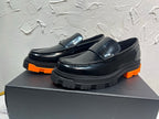 Black leather loafers with orange outsole and metal buckle detail, side view pair