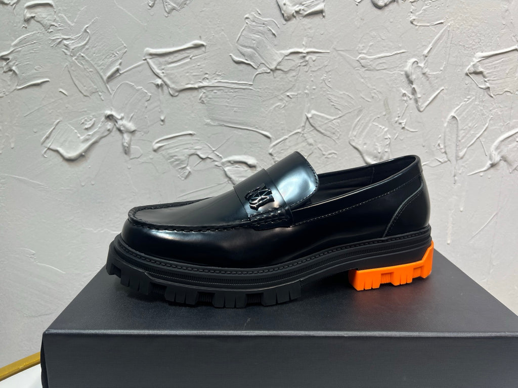 Black leather loafer with orange tread sole and metal buckle detail, side profile