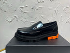 Black leather loafer with orange tread sole and metal buckle detail, side profile