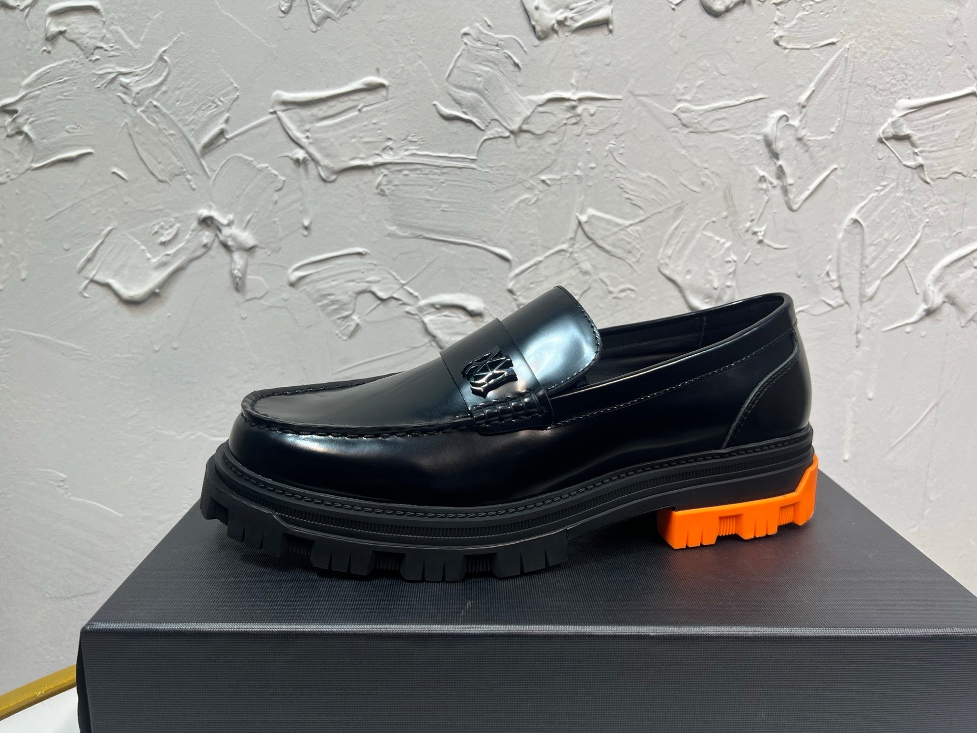 Black leather loafer with orange tread sole and metal buckle detail, side profile
