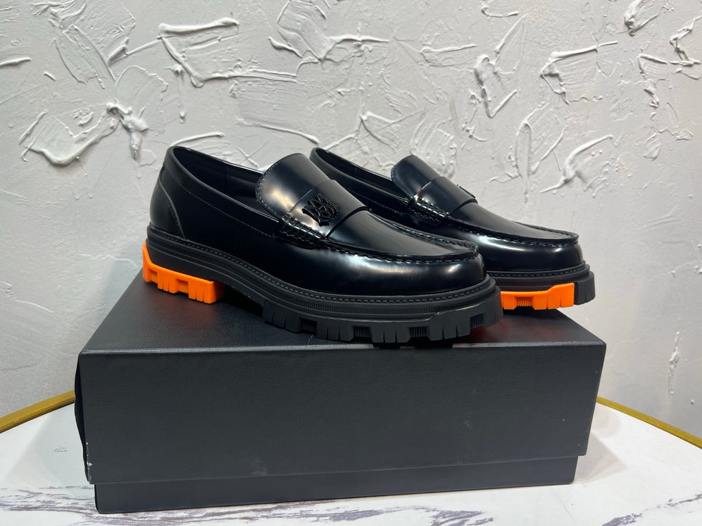 Black leather loafer pair with orange tread sole and metal buckle detail, angled view