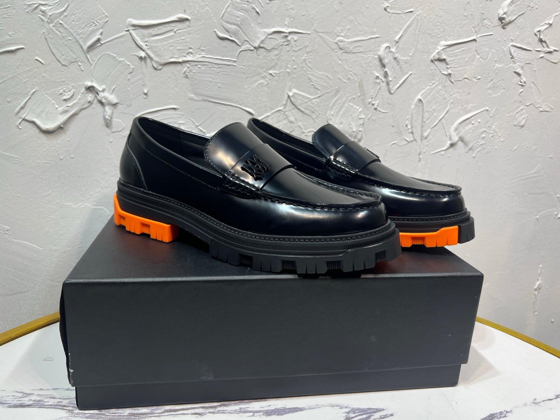 Black leather loafer pair with orange tread sole and metal buckle detail, angled view