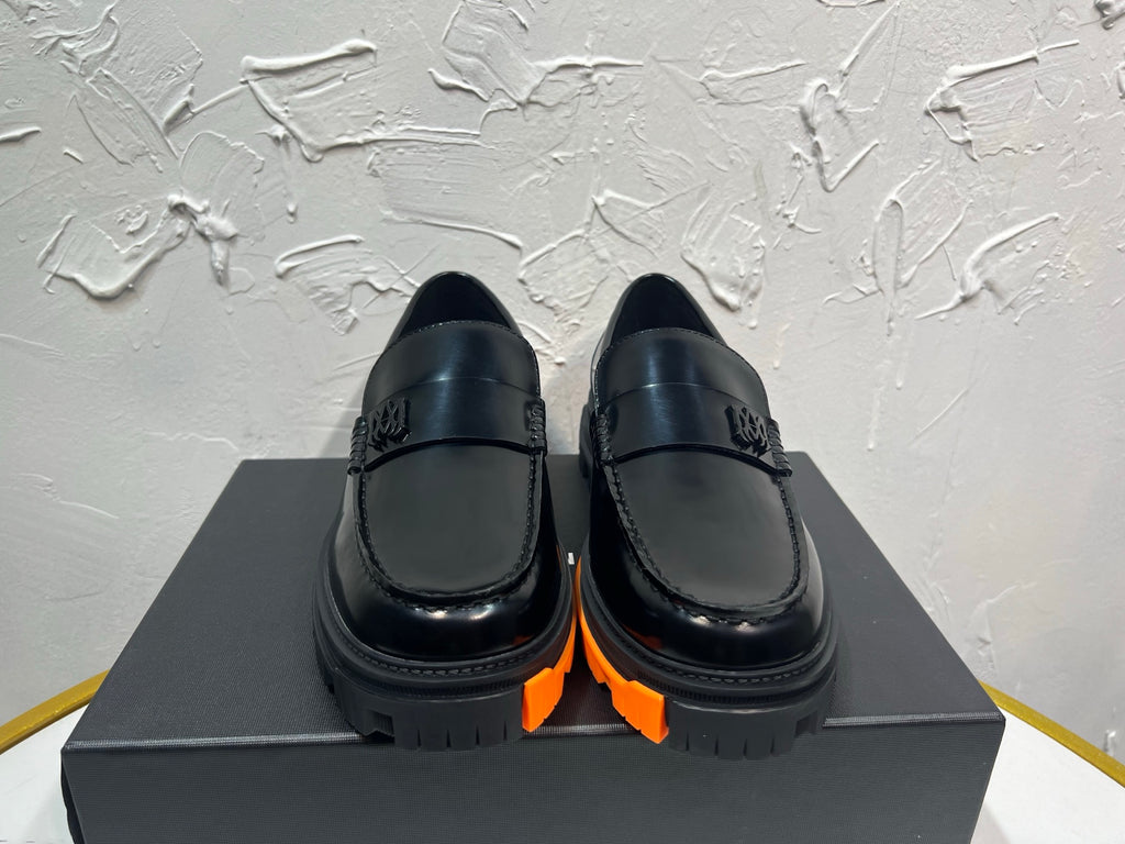 Black leather loafers with orange tread sole and metal buckle detail, pair on box