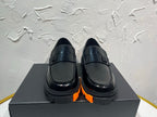 Black leather loafers with orange tread sole and metal buckle detail, pair on box