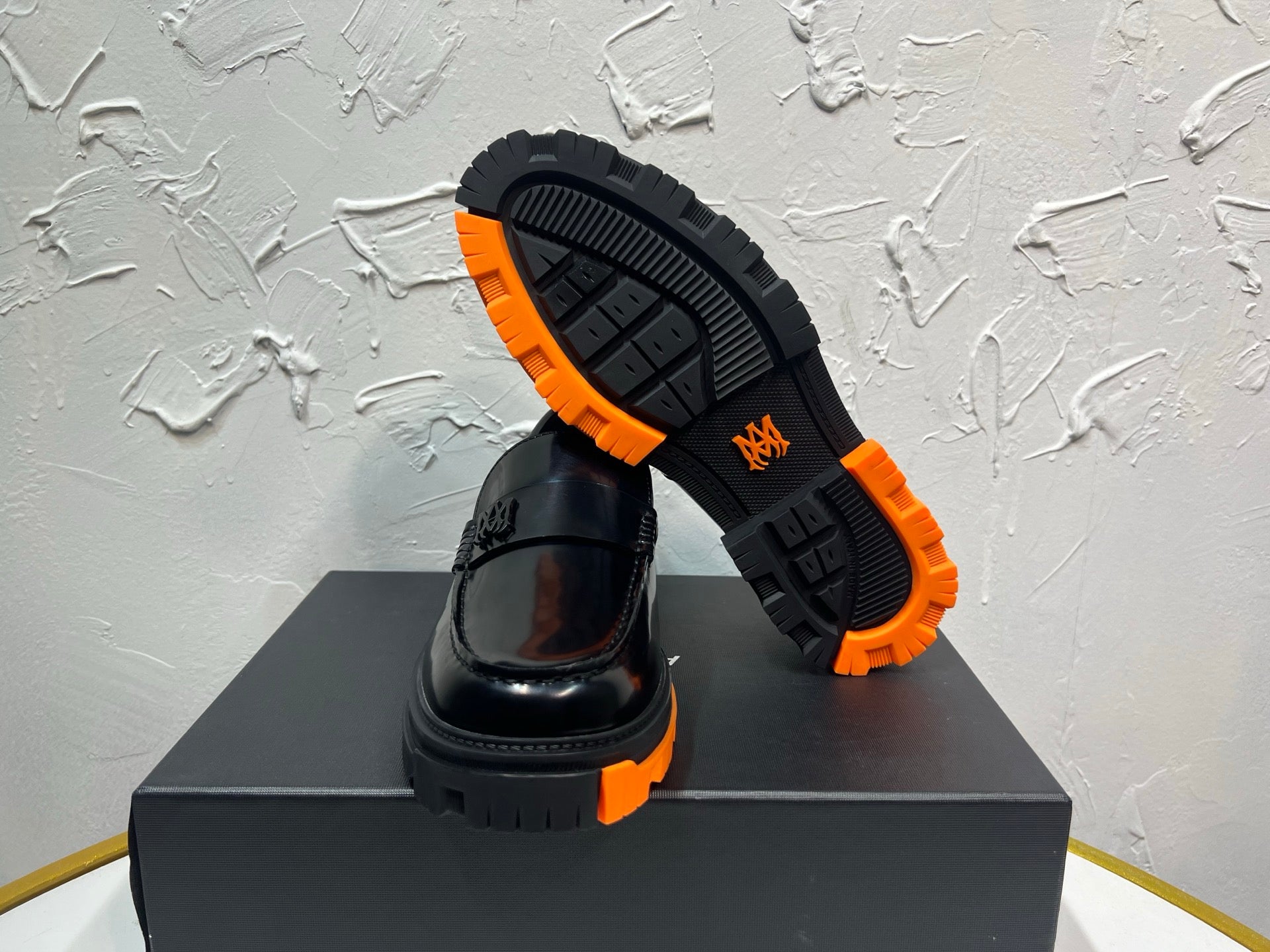 Black leather loafers with orange tread outsole, one showing bottom tread pattern