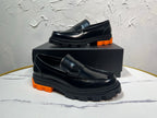 Black leather loafer with orange tread sole and metal buckle detail, single shoe on box