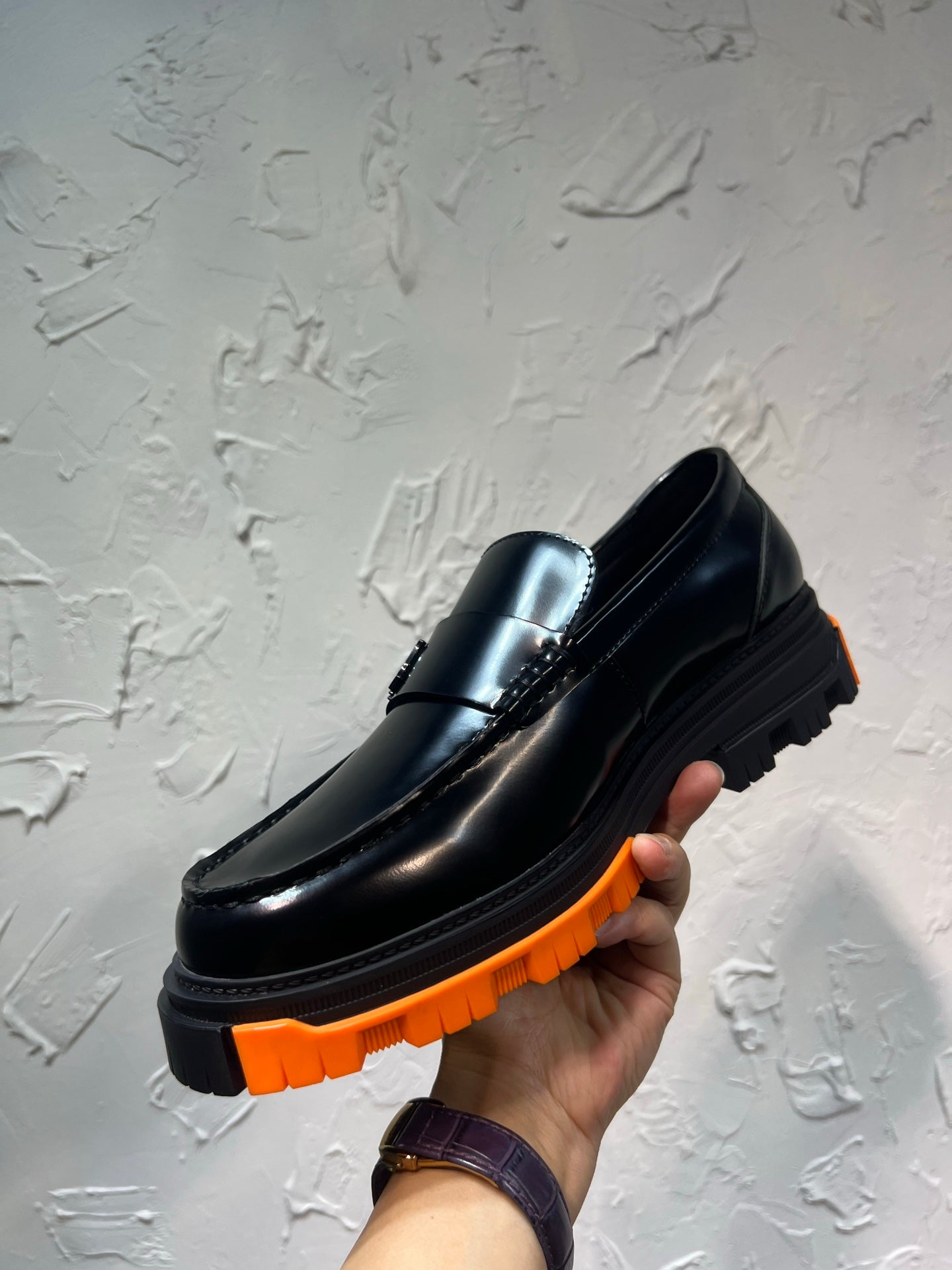 Black leather loafer with orange tread sole, close-up showing metal buckle detail