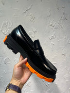 Black leather loafer with orange tread sole, hand-held side view