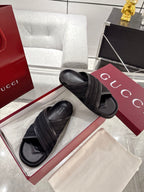 Black Gucci slide sandals with embossed pattern wide strap and open toe.