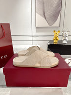 Beige Gucci slide sandals with textured logo-style straps on a red shoebox