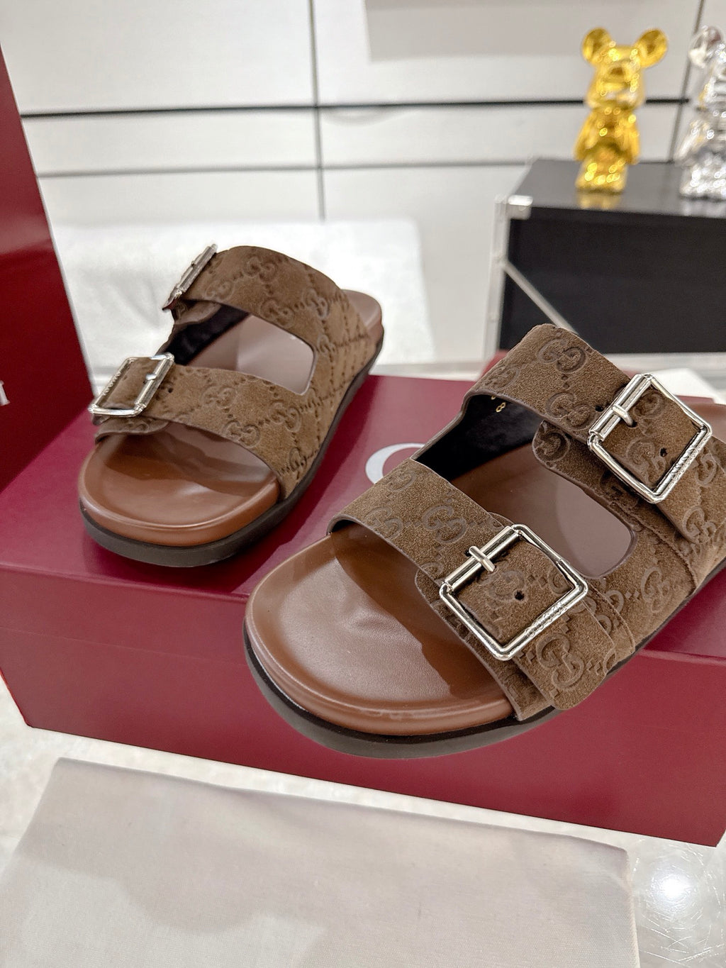 Brown logo-print slide sandals with two silver-tone buckles, shown side by side