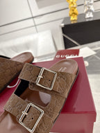 Brown logo-print slide sandals with two silver-tone buckle straps on red display box
