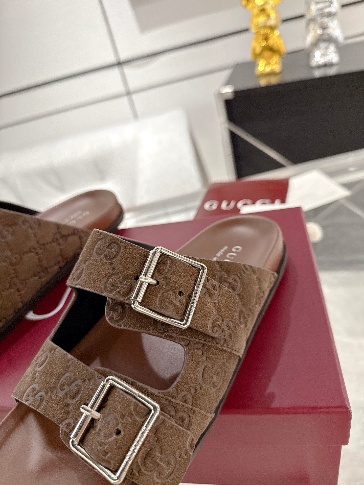 Brown logo-print slide sandals with two silver-tone buckle straps on red display box