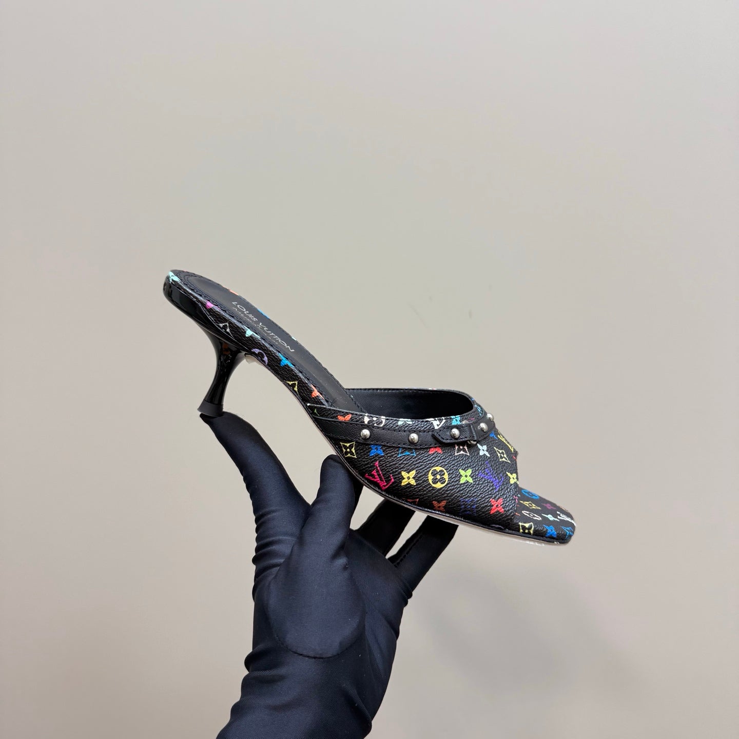Louis Vuitton women's mule heel held in hand, multicolor logo print on black