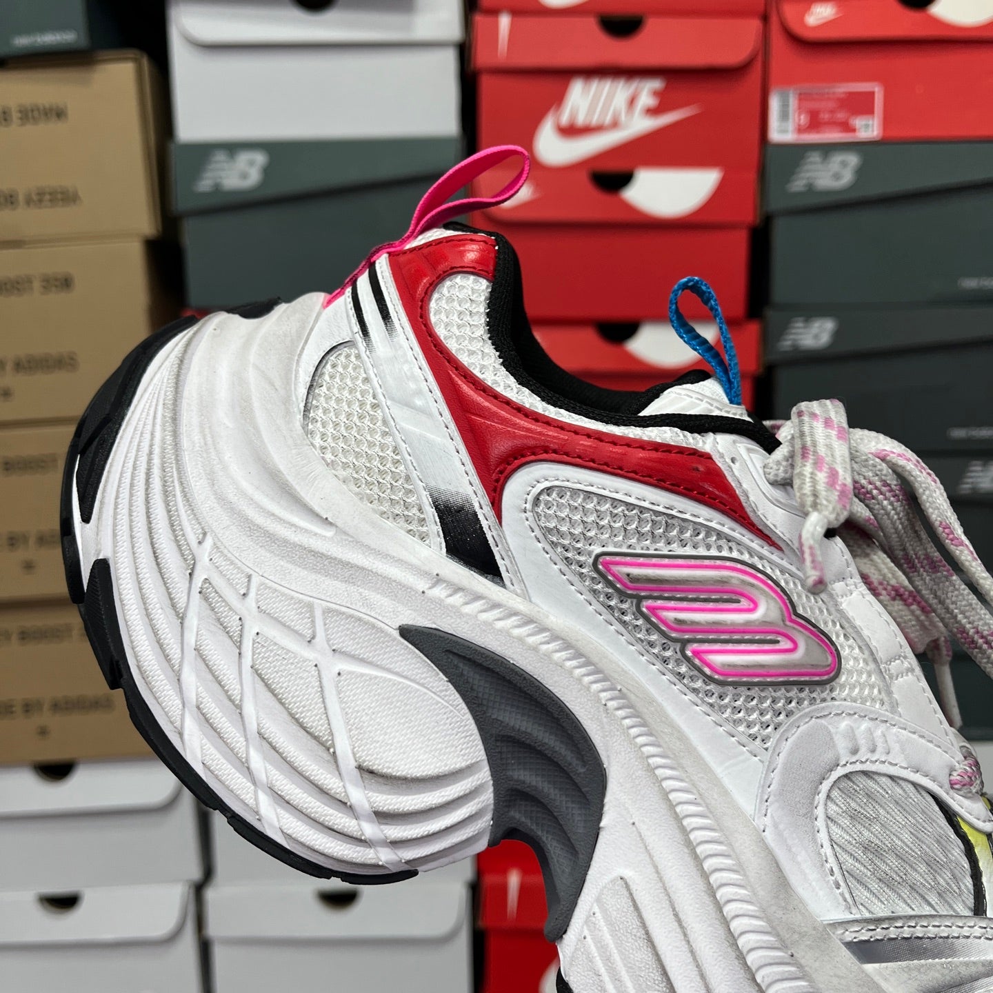 Unisex sneaker side view in white with red trim and pink logo detail.