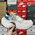 Unisex sneaker angled side view in white with blue and pink heel accents.