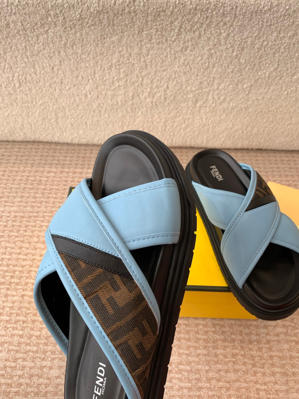 Light blue slide sandals with black strap trim and dark monogram footbed