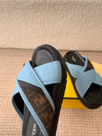 Light blue slide sandals with black strap trim and dark monogram footbed