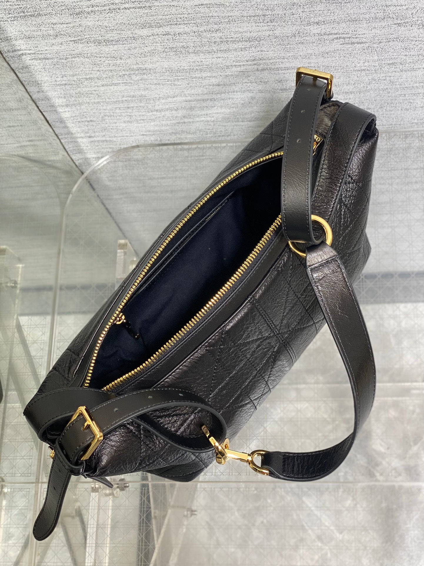 Black Dior crossbody bag with open top, gold zipper, and adjustable strap